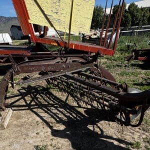 LOT 3 7 - Montana Auctions by Kevin Hill Rusty old hay rake with curved iron frame and tines, resting on wooden blocks in a rural yard.