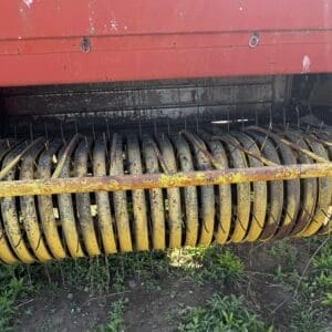 LOT 4 2 - Montana Auctions by Kevin Hill Rusty yellow curved tines of a farm baler reel beneath a red metal housing, dirty and weathered.
