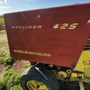 LOT 4 3 - Montana Auctions by Kevin Hill Red Hayliner 425 bale wagon with a yellow frame and wheel, on a grassy field under a clear blue sky.