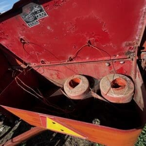 LOT 4 4 - Montana Auctions by Kevin Hill Red metal trailer with exposed orange wires and two spool-like cable reels, outdoors on dirt, warning triangle on the side