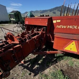 LOT 4 5 - Montana Auctions by Kevin Hill Red New Holland agricultural implement with a plow frame, parked on dirt with mountains in the background (informational, shows machinery used for tilling).