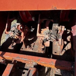 LOT 4 7 - Montana Auctions by Kevin Hill Close-up of rusted tractor hitch linkage with worn bolts and clamps on an orange metal frame.