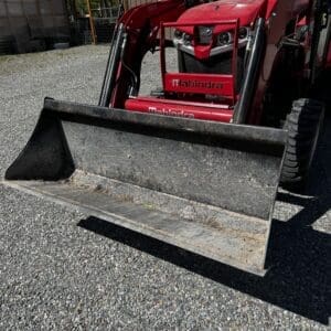 LOT 5 4 - Montana Auctions by Kevin Hill Red Mahindra compact tractor with a front-end loader bucket parked on gravel outdoors, with a shed and trees in the background.