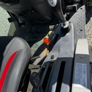 LOT 5 9 - Montana Auctions by Kevin Hill Inside a heavy equipment cab: joystick control with a red button, a black seat with a red stripe, and a 'To Start Engine' label on the console.