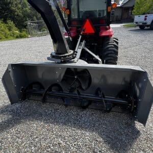 LOT 7 4 - Montana Auctions by Kevin Hill Red Mahindra tractor with a large front-mounted snow blower/auger attachment on a gravel driveway, mountains and trees in the background.