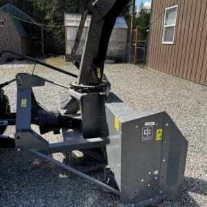 LOT 7 7 - Montana Auctions by Kevin Hill Large industrial wood chipper attachment outdoors, with a tall angled black chute and gray base housing, on a gravel area near buildings.
