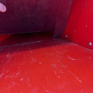 LOT 8 4 - Montana Auctions by Kevin Hill Close-up of a red metal surface with a brown flap being lifted by a finger; visible scratches and a small warning sticker in the corner.