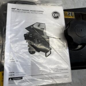 LOT 8 7 - Montana Auctions by Kevin Hill Manual for a DR Self-Feeding Wood Chipper (Premier 375) inside a plastic bag, photographed on a workshop floor.