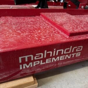 LOT 9 2 - Montana Auctions by Kevin Hill Red industrial machinery with a white 'machina IMPLEMENTS' logo, resting on a wooden block in a workshop setting.