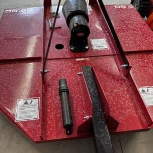 LOT 9 4 - Montana Auctions by Kevin Hill Close-up of a red automotive lift base in a workshop, featuring a black drive shaft and hitch-like component in the center with warning labels visible.