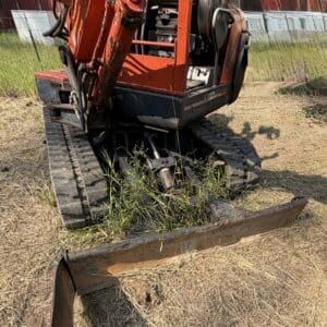 1 3 - Montana Auctions by Kevin Hill Orange mini excavator with a rusted front bucket sits on dry grass in a rural yard.