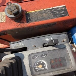 1 4 - Montana Auctions by Kevin Hill Operator dashboard of a red construction machine with a circular tachometer, gauges, and levers visible amid a dusty panel.