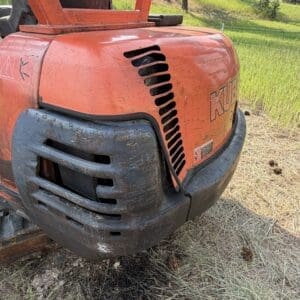 1 5 - Montana Auctions by Kevin Hill Close-up of an orange Kubota mini excavator front with a dirt-splattered black bumper on a grassy outdoor site