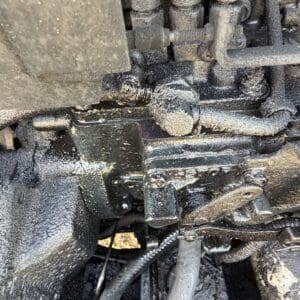 1 5 - Montana Auctions by Kevin Hill Close-up of a dusty, greasy engine area with hoses, fittings, and a metal bracket.