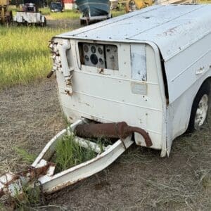 10 1 - Montana Auctions by Kevin Hill White utility trailer with a rusted hitch and exposed control panel, sitting on dry grass.
