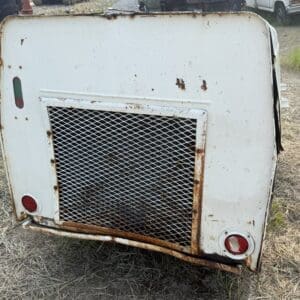 10 2 - Montana Auctions by Kevin Hill Rear view of a weathered white metal trailer with a rusted mesh grate and round red taillights.