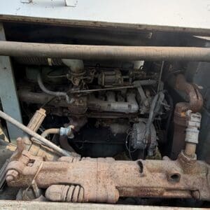 10 4 - Montana Auctions by Kevin Hill Open hood reveals a rusted engine and drive train with exposed pipes in an old heavy vehicle.
