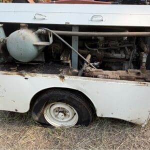 10 5 - Montana Auctions by Kevin Hill Old white portable generator with an exposed engine and visible rust, mounted on a small trailer outdoors on dry grass.