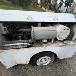 10 6 - Montana Auctions by Kevin Hill Rusty portable generator with exposed engine mounted on a white trailer, outdoor grassy area in the background and worn wheels visible, likely unused or awaiting repair.