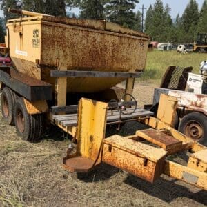11 1 - Montana Auctions by Kevin Hill Rusty yellow cement mixer on a trailer in a field, with worn metal supports and tires in the background.