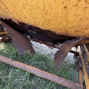 11 3 - Montana Auctions by Kevin Hill Yellow industrial vehicle/tactory tank with severe rust and torn underside, exposing corroded metal and green grass beneath.