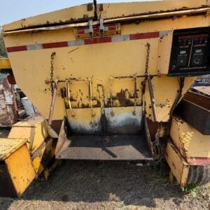 11 4 - Montana Auctions by Kevin Hill Rusted yellow industrial hopper with loading chute and hand levers, on an outdoor machine, with chipped paint and dirt buildup on the ground