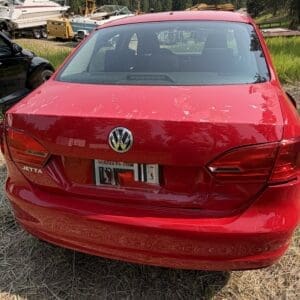 13 2 - Montana Auctions by Kevin Hill Rear view of a red Volkswagen Jetta with a dented bumper parked on dry grass, boats and boat trailers in the background.