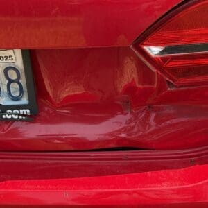 13 3 - Montana Auctions by Kevin Hill Red car rear with visible dent and scuffed bumper near taillight; license plate partially visible on left side.