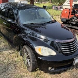 14 1 - Montana Auctions by Kevin Hill Black Chrysler PT Cruiser-style SUV parked on a grassy lot with orange construction equipment in the background.