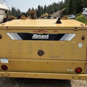 15 1 - Montana Auctions by Kevin Hill Yellow Allmand industrial generator unit viewed from the back, with vents, gauges, and a fuel cap; boats and construction equipment visible in a yard.