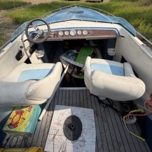 16 3 - Montana Auctions by Kevin Hill Open boat cockpit with two white-blue seats, dusty dashboard, steering wheel, and items cluttering the deck.【image】