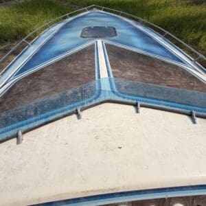 16 6 - Montana Auctions by Kevin Hill Front view of a blue vintage boat bow resting on dry ground with grass in the background, seen from above.