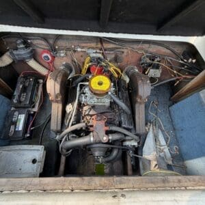 16 7 - Montana Auctions by Kevin Hill Inboard boat engine in a wooden engine bay, with a yellow air filter, red wires, and a battery to the left. Rusty metal and hoses surround the motor.