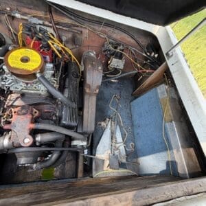 16 9 - Montana Auctions by Kevin Hill Open engine compartment of an old boat or vehicle showing a rusted engine, yellow air filter, and a tangle of wires and hoses under a hatch.