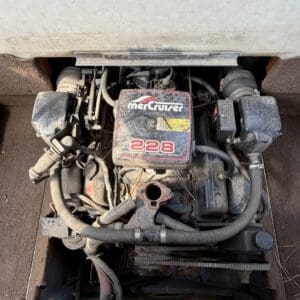 17 3 - Montana Auctions by Kevin Hill Boat engine showing a MerCruiser 228 in a dusty engine compartment, with hoses and belts visible around the unit.