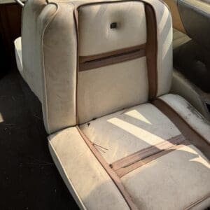 17 4 - Montana Auctions by Kevin Hill Worn beige car seat with brown piping inside an old vehicle, showing dirt and a torn cushion seam.
