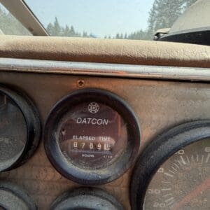 17 8 - Montana Auctions by Kevin Hill Old dusty car dashboard featuring a round Datcon elapsed-time meter showing 070404 hours, with other gauges and a dusty windshield in the background.