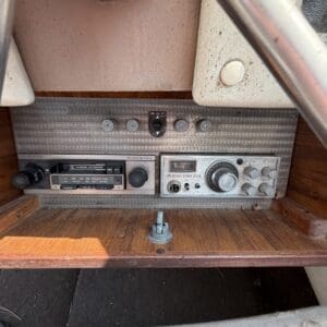 17 9 - Montana Auctions by Kevin Hill Close-up of a vintage radio console on a worn wooden dashboard, with multiple knobs and a central dial.