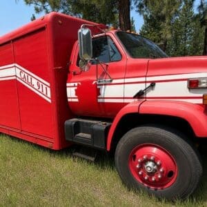 18 2 - Montana Auctions by Kevin Hill Red hazmat operations rescue truck on a grassy field with white stripes and 'CALL 911' lettering visible on the side.