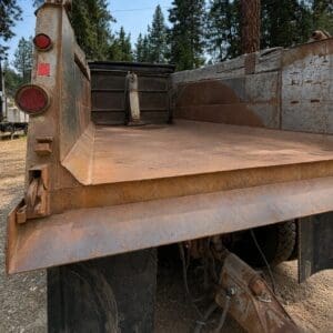 19 1 - Montana Auctions by Kevin Hill Rusty dump truck bed viewed from rear, with red taillights and weathered metal panels in an outdoor setting.