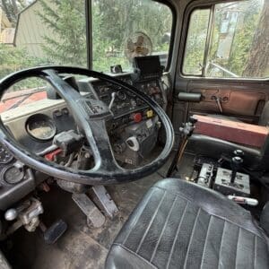 19 4 - Montana Auctions by Kevin Hill Interior of a dusty, well-used truck cab showing a large steering wheel, grimy pedals, and a cluttered dashboard with gauges and switches.