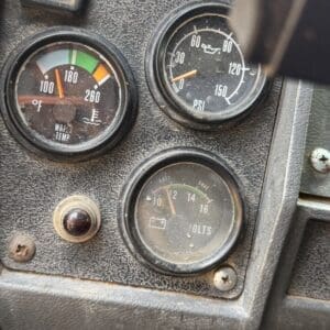 19 8 - Montana Auctions by Kevin Hill Close-up of a dusty vehicle dashboard with three gauges: water temperature (left), oil pressure (top-right), and voltmeter (bottom).