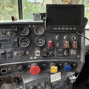 19 9 - Montana Auctions by Kevin Hill Dashboard of a heavy-duty truck with multiple gauges, switches, and a touchscreen monitor; a large NAPA fan sits above the dash in the windshield view.