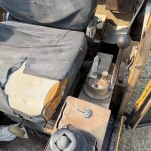 2 11 - Montana Auctions by Kevin Hill Worn construction vehicle cab interior with dusty fabric seat, rusty metal panels, and a gear lever nearby.