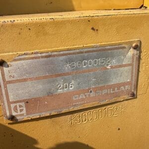 2 3 - Montana Auctions by Kevin Hill Close-up of a worn metal identification plate on a yellow Caterpillar machine, showing model 206 and serial number *3GC00152*.