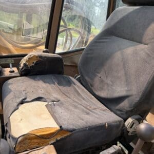2 7 - Montana Auctions by Kevin Hill Old tractor cab interior with a ripped, torn driver’s seat exposing yellow foam and dusty surfaces nearby.