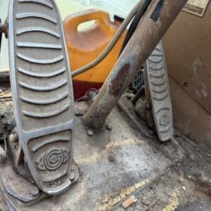 2 8 - Montana Auctions by Kevin Hill Close-up of two textured foot pedals on a dusty, rusted construction machine with an orange container in the background.