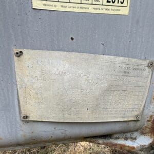 20 4 - Montana Auctions by Kevin Hill Weathered metal data plate on a blue-gray surface with rust, showing model 'END DUMP 1230-2' and various vehicle specifications (numbers and tire sizes) faded by time.