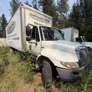 22 1 - Montana Auctions by Kevin Hill White box truck stuck in tall weeds beside a forested area; logos read Gulf-Great Lakes on the side.