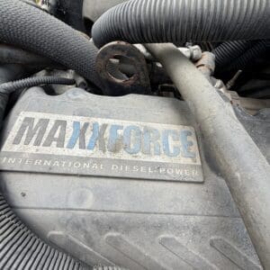 22 5 - Montana Auctions by Kevin Hill Close-up of a dusty diesel engine cover with a MaxForce badge that reads 'MAXFORCE International Diesel Power' surrounded by hoses and metal components.